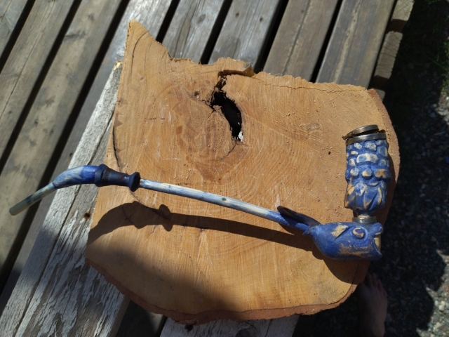 Blue pipe on piece of wood.
Pioe has long stem and curvy bit stem is connected to whale looking part and Bowl that looks like water coming from blow hole is connected on top of whale