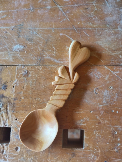 Wood spoon on table. Spoon is short and handle ends to hear shape.