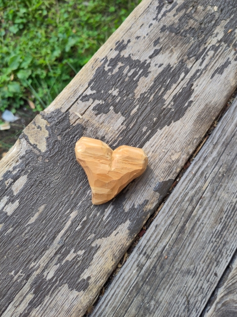 Half ready wooden heart on wood floor. And there's some foliage on the corner