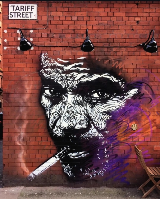 Streetartwall. A very cool mural of a man smoking was sprayed on the red brick exterior wall of a bar in Manchester. The head of a man with a full beard and a smoking cigarette in the corner of his mouth was "drawn" with black spray paint on a white background. In fact, this mural consists of an infinite number of small black lines and is fantastically detailed. 
The man with the wrinkles on his forehead looks at the viewer almost hypnotically. (Note: Incidentally, the face strongly resembles that of the artist)
Info: C215 is the artist name of Christian Guémy, a famous French street artist, painter and curator from Paris. He became known for his beautiful cat paintings sprayed with stencils on public walls and has since become an important figure in the French art scene, showered with medals and awards.