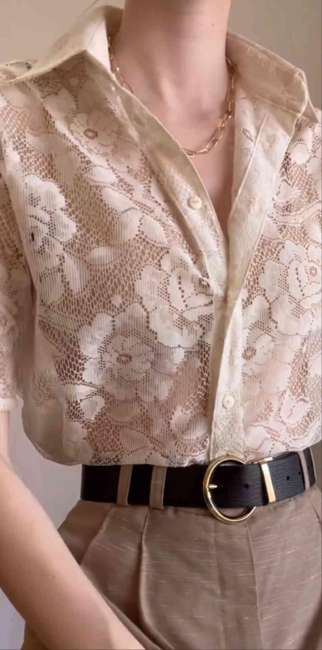 Person wearing a cream lace floral top, brown pants, and a black belt with a gold buckle.