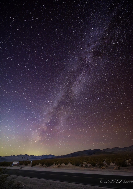 A breathtaking view of the Milky Way stretches across a clear night sky, revealing countless stars over the quiet desert of Death Valley, California. The horizon shows distant mountains silhouetted against the subtly colorful glow of the sky.
The vertical composition is particularly effective in showcasing the grandeur of the Milky Way against the Death Valley landscape.
December 2024