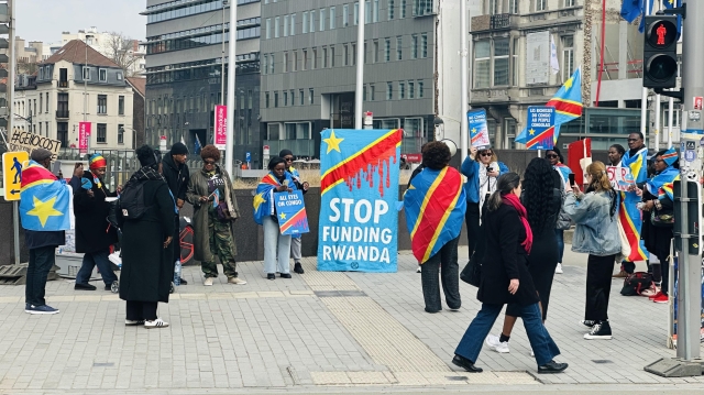 A small but loud group of Congolese protesters on a city sidewalk carrying banners with various pro-Congo and anti-Rwanda slogans. A big sign in the middle says: Stop Funding Rwanda. 