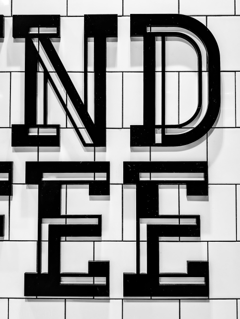 Black stylized bold letters "ND EE". The background's grid pattern of white tiles and dark grout provides a strong contrast, emphasizing the shapes of the letters. 