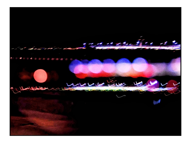 Fotografía abstracta desde la ventanilla del avión en la pista de despegue/aterrizaje. Sobre un fondo negro (es de noche) diferentes exposiciones de una de las terminales del aeropuerto desde lejos: vemos líneas de luces, jugando con varias exposiciones, el foco y algunas largas exposiciones algunas luces están desenfocadas, otras dibujan líneas al estar el avión ya moviéndose