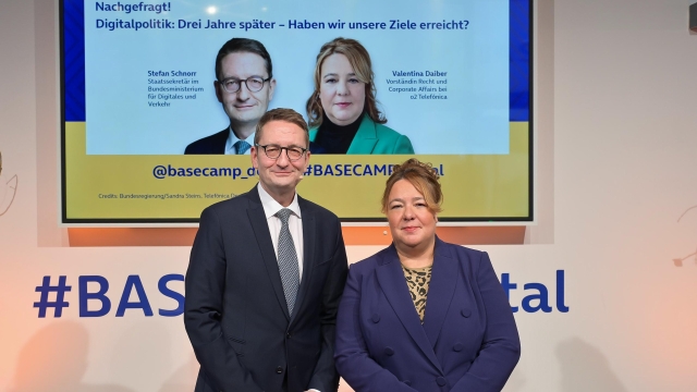 ©BASECAMP | Foto: Henrik Andree. Staatssekretär Stefan Schnorr und Valentina Daiber, Vorständin Recht und Corporate Affairs bei o2 Telefonica lächeln in die Kamera. Im Hintergrund weist eine Präsentation auf den Titel der BASECAMP-Debatte hin: "Digitalpolitik: Drei Jahre später - Haben wir unsere Ziele erreicht?".