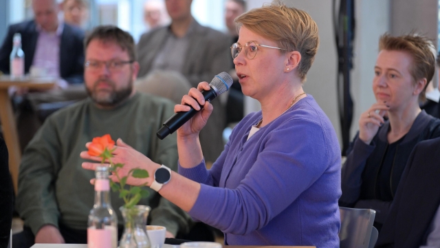 ©BASECAMP | Foto: Henrik Andree. Das Foto zeigt einen Teil des Publikums der BASECAMP-Debatte. Eine Frau hält ein Mikrofon in der Hand und gestikuliert, um das Gesagte zu unterstreichen.