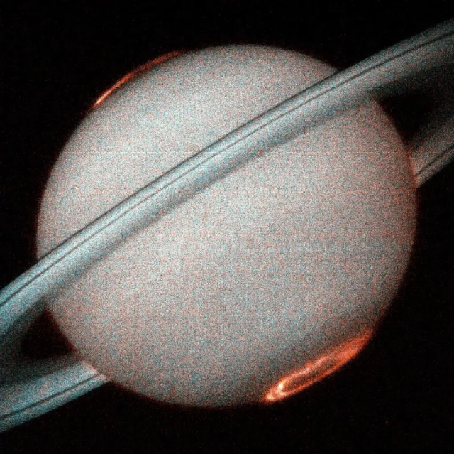 A grainy image of Saturn, taken by an imaging spectrograph, showing the planet in white, the rings in gray, and the aurorae at both poles in orange.