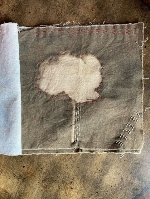 A tea-stained cyanotype that is embroidered with red around the flower and beige to look like a tree trunk. There is red stitching along the top and some beige diagonally along the lower right.