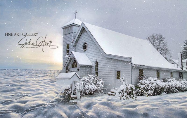 Little white chapel in heavy snowstorm, a beacon of light. Sun is trying to peek thru the clouds. Photo is in tones of white, gray and pale blue. From the Fine Art Gallery of Shelia Hunt.